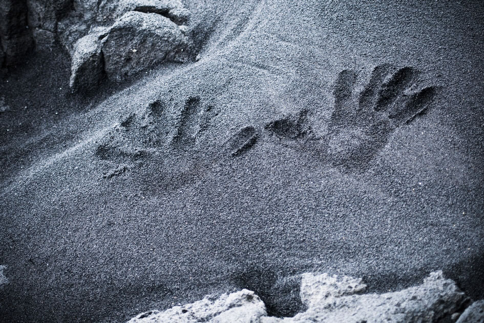 Hands in the black sand at Punalu’u Beach Park, the Big Island of Hawaii